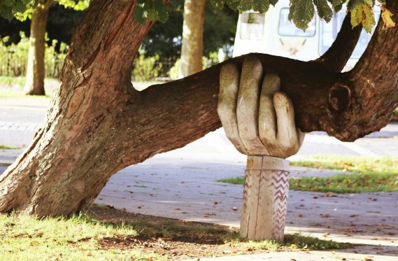 Large tree limb being supported by a wooden carving of a hand